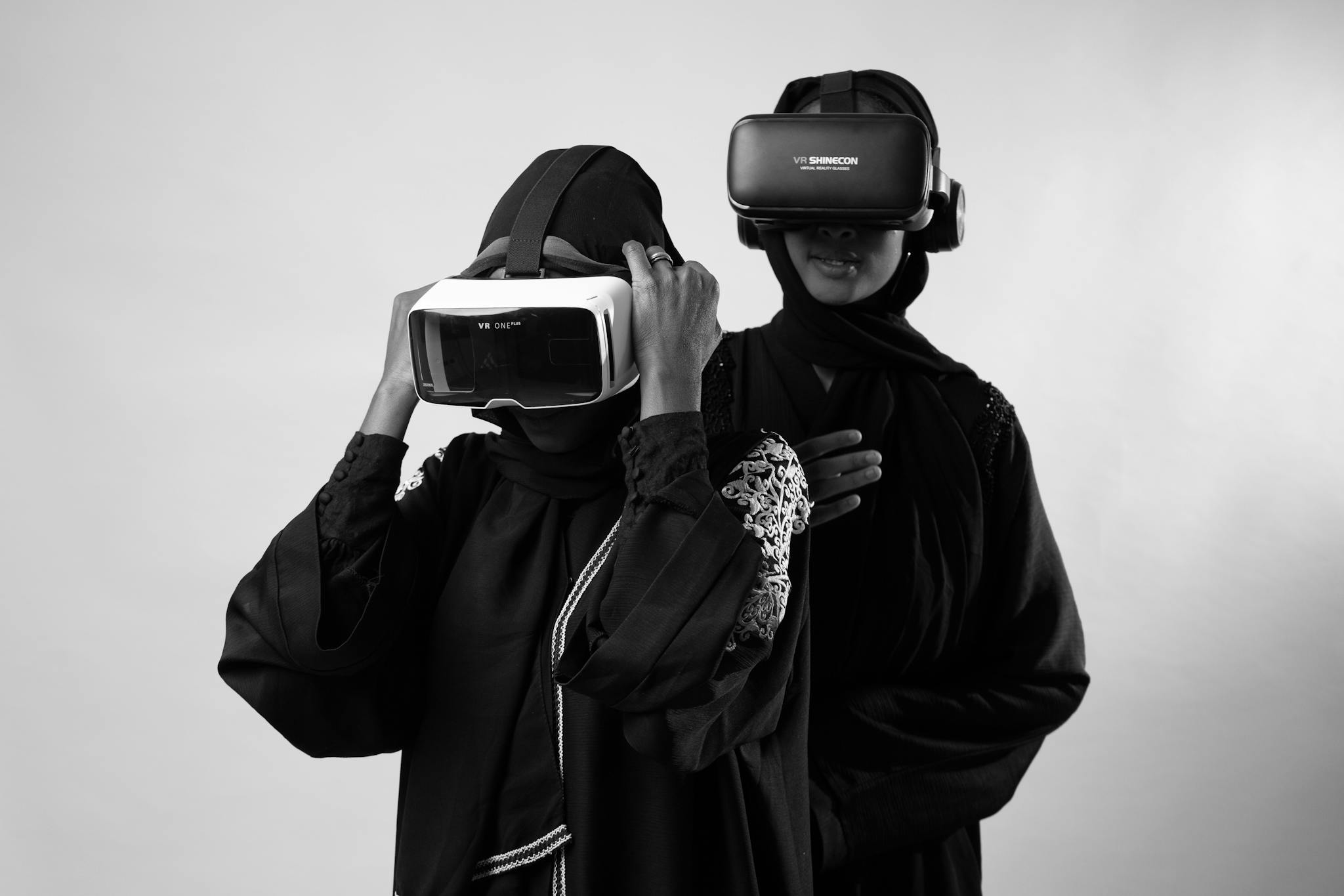 Black and white photo of women in hijabs using VR headsets in a studio environment, showcasing modern technology.