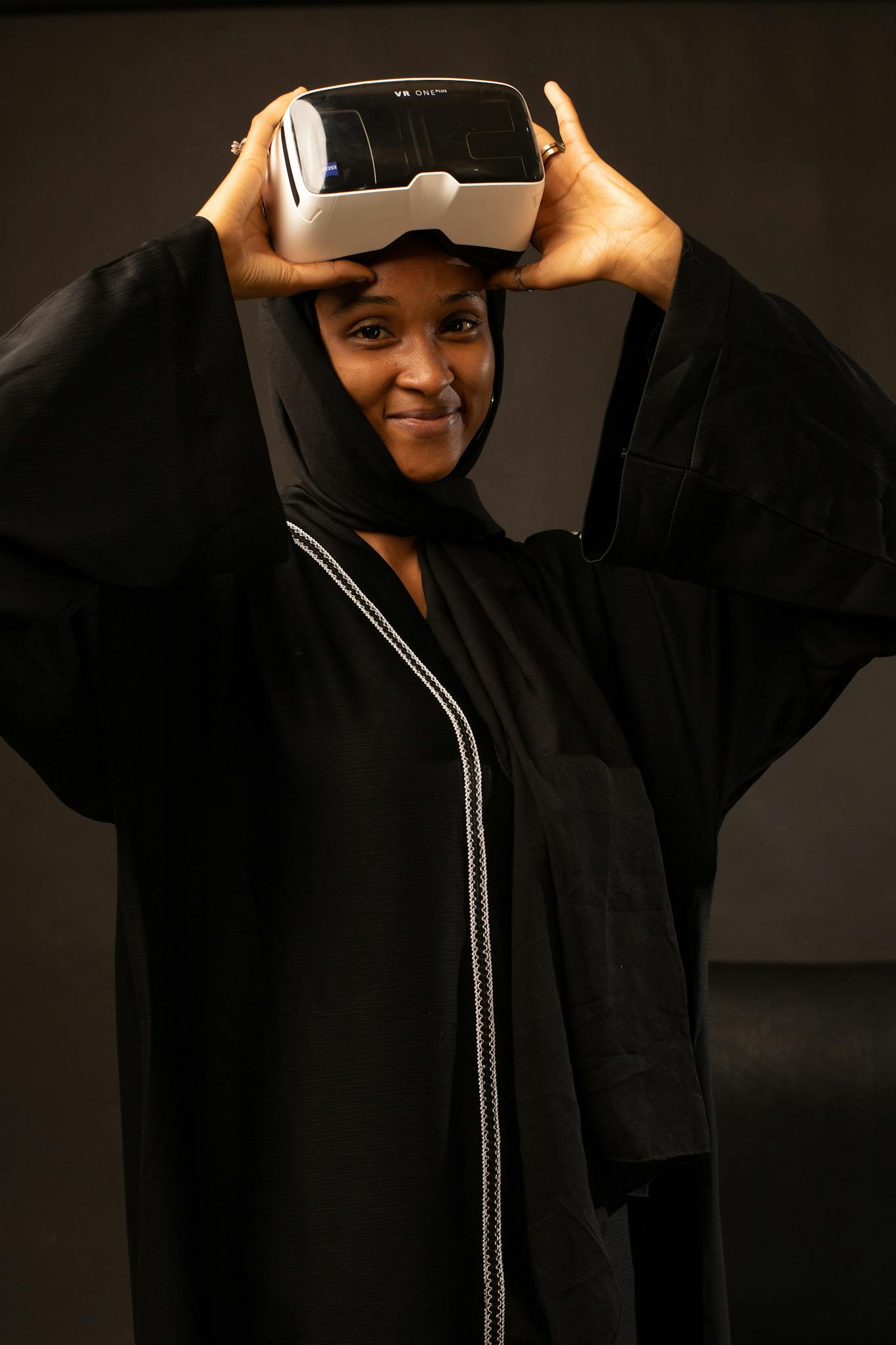 Smiling woman in traditional hijab using VR headset indoors.