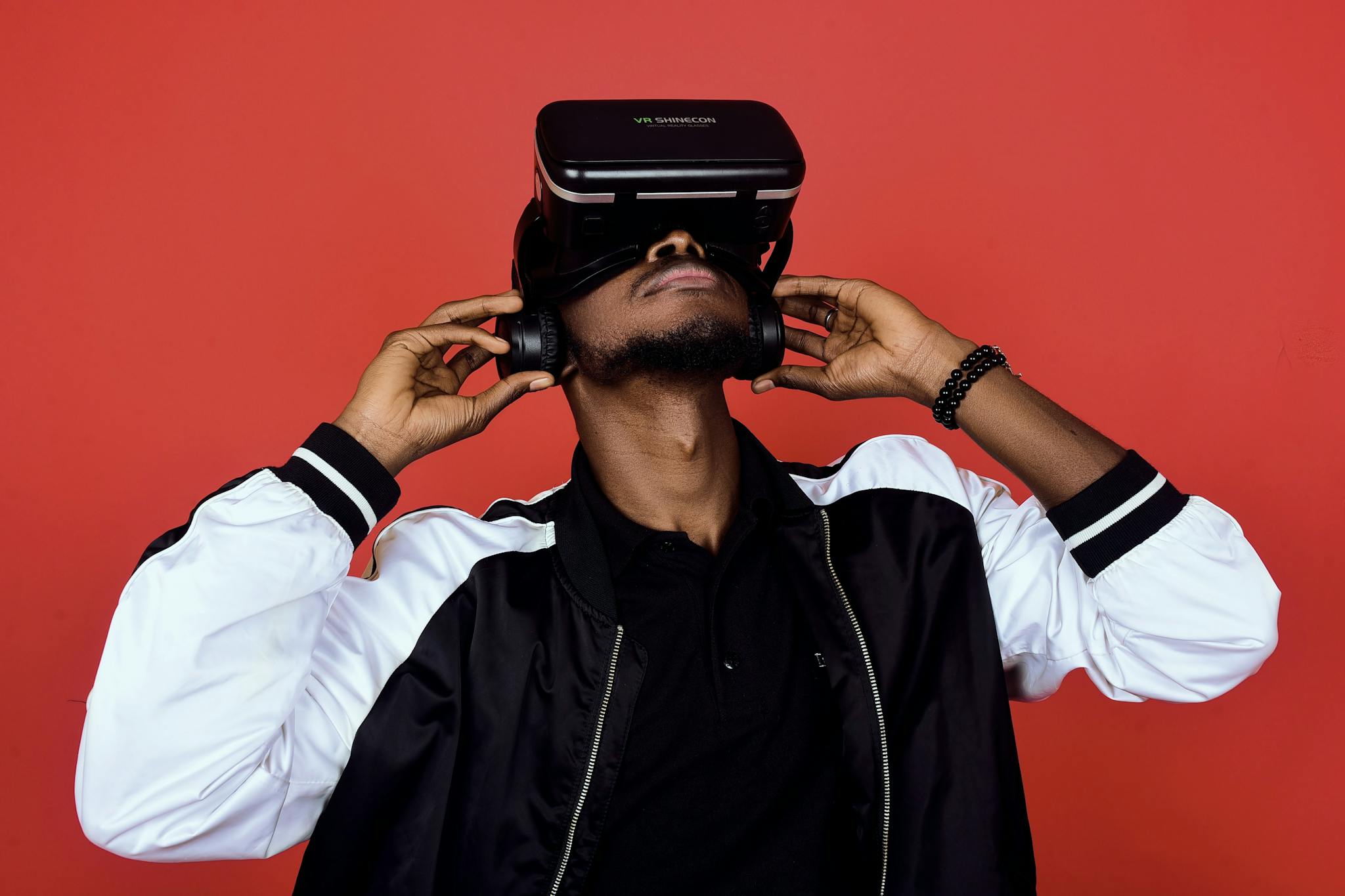 Stylish man wearing VR headset and headphones on a vibrant red background.